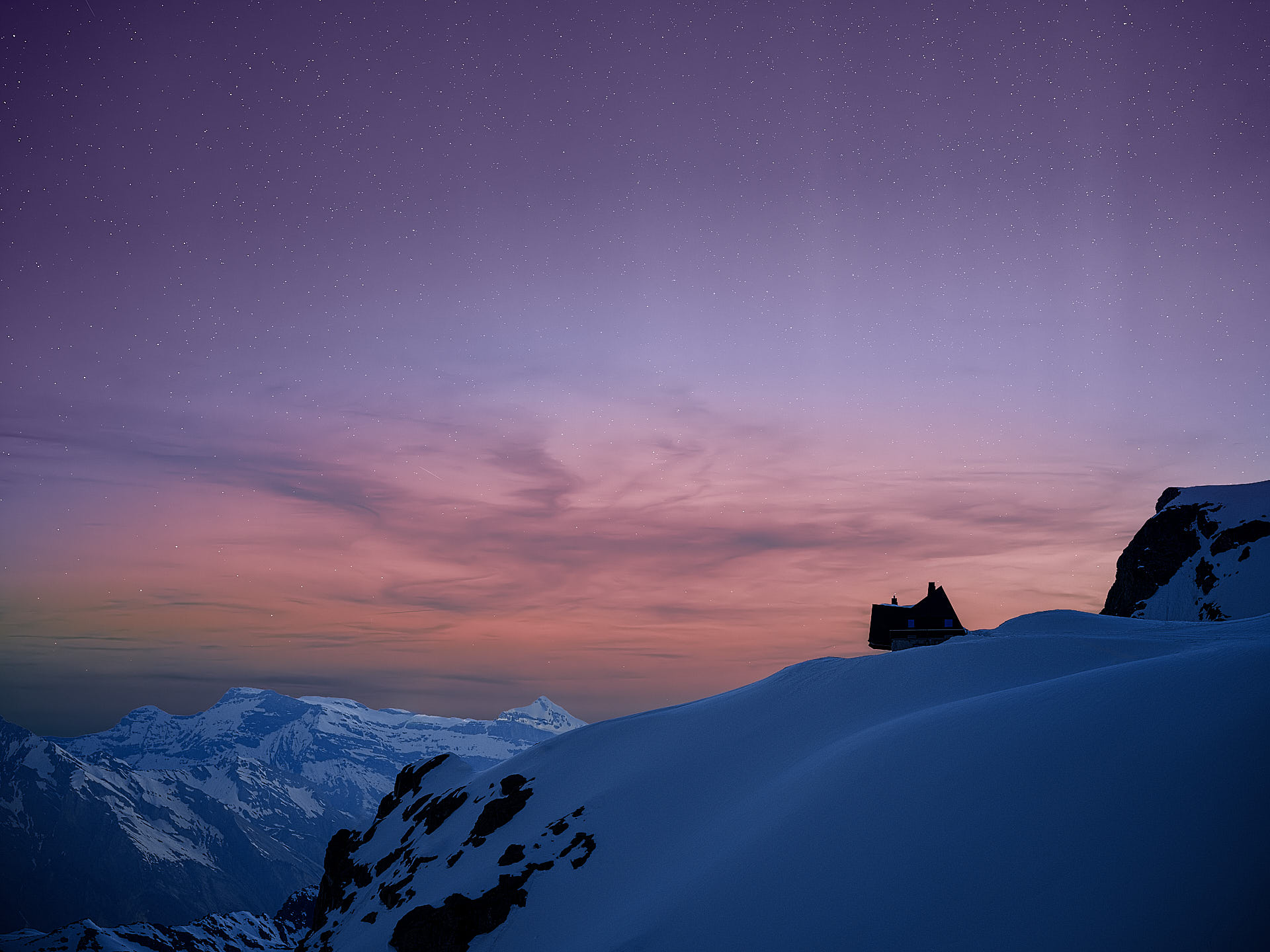 Dramatic twilight silhouette of Cabane Tortin luxury ski chalet at 3,000 metres with warm interior lighting glowing against a deep blue Alpine sky